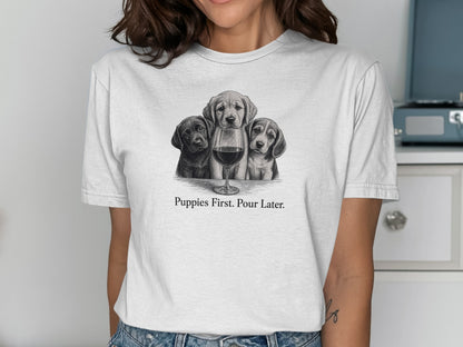 White t-shirt with three puppies and a glass of wine graphic and text "Puppies First. Pour Later."