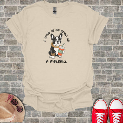 French bulldog wearing a gold chain holding a coffee cup, text reads "A miss is as good as a molehill".