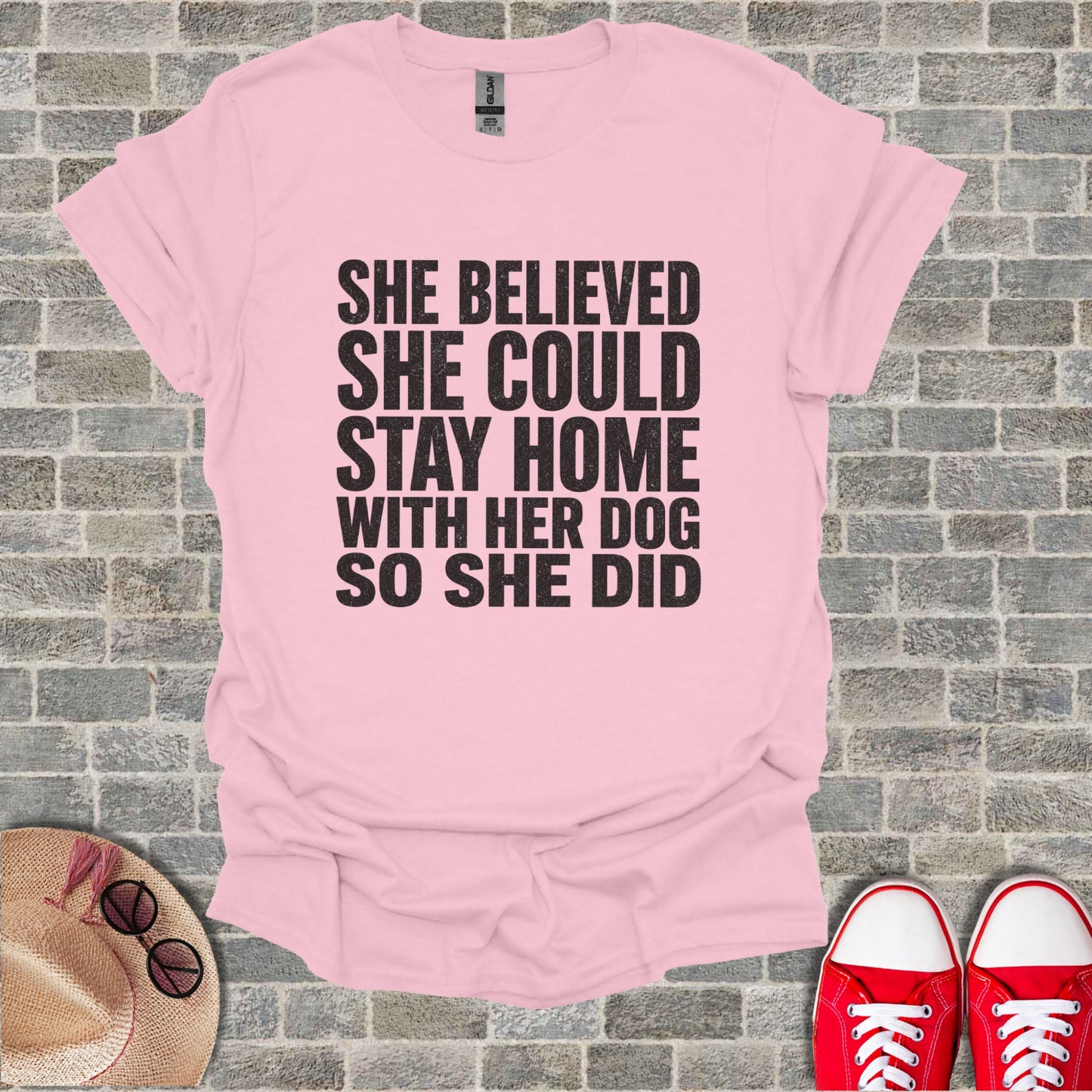 Pink t-shirt with black text: "She believed she could stay home with her dog so she did."