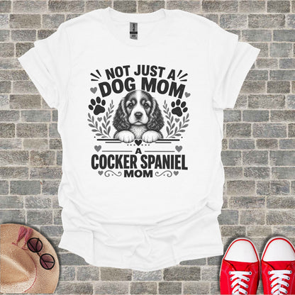 White t-shirt with "NOT JUST A DOG MOM A Cocker Spaniel MOM" text and dog graphic.