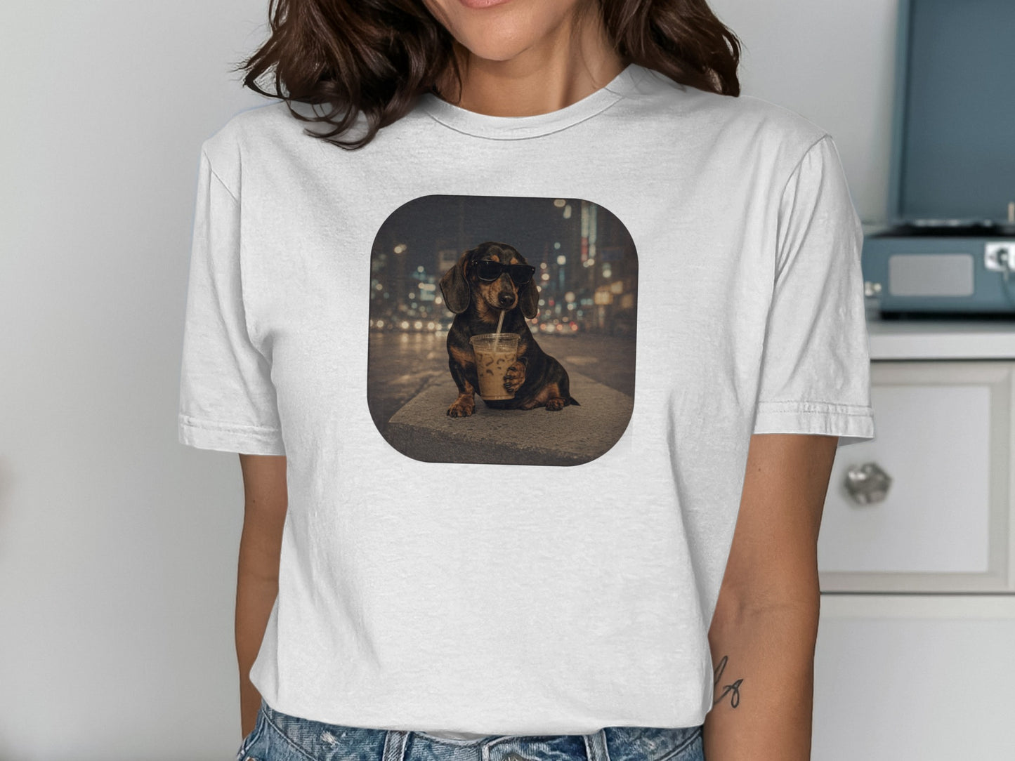 Dachshund wearing sunglasses drinks from iced coffee with blurry city lights background.