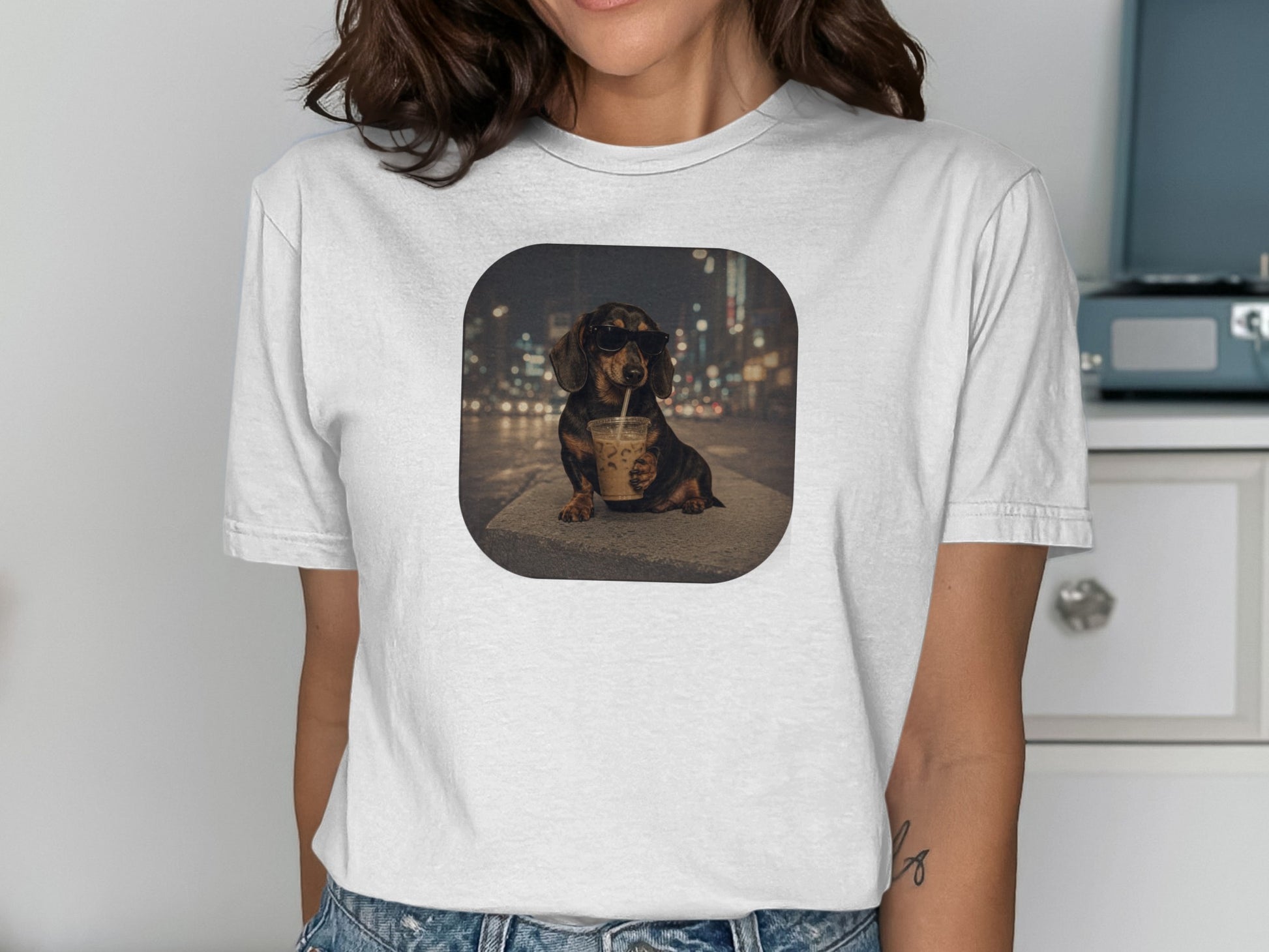 Dachshund wearing sunglasses drinks from iced coffee with blurry city lights background.