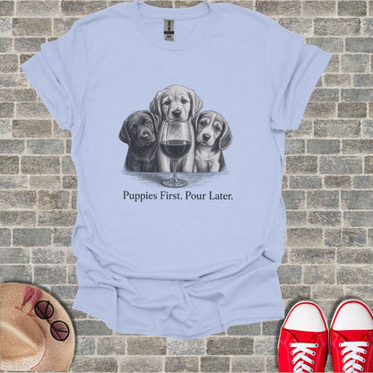Light blue t-shirt with three puppies and a glass of wine, text says "Puppies First. Pour Later."