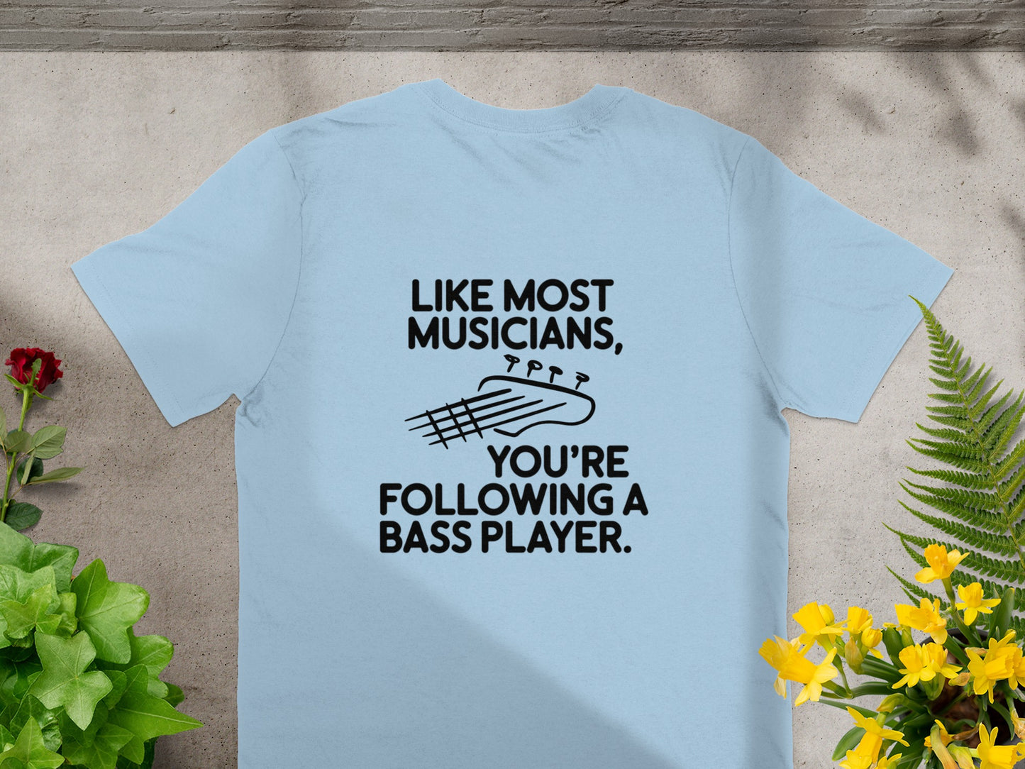 Light blue t-shirt with black text and bass guitar graphic: "LIKE MOST MUSICIANS, YOU'RE FOLLOWING A BASS PLAYER."