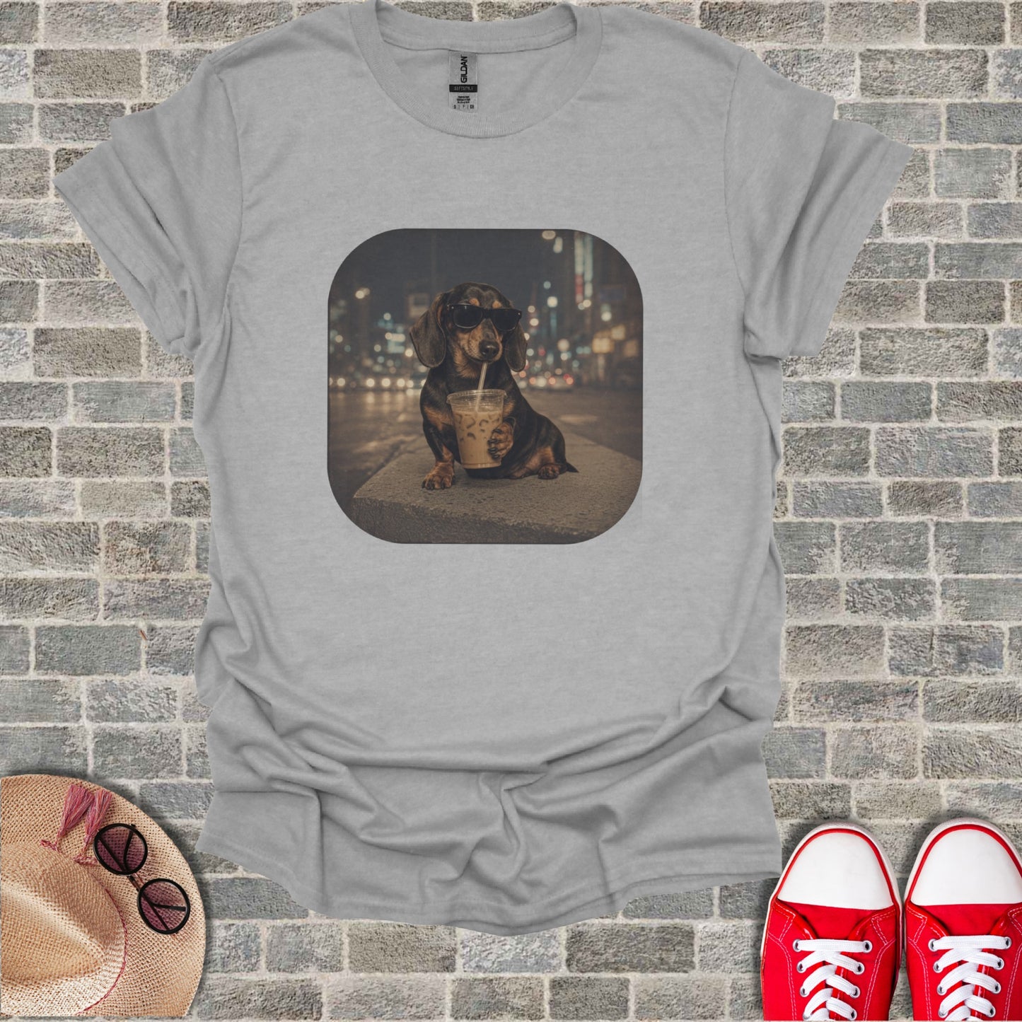 Dachshund wearing sunglasses drinks from a coffee cup with cityscape background on t-shirt.