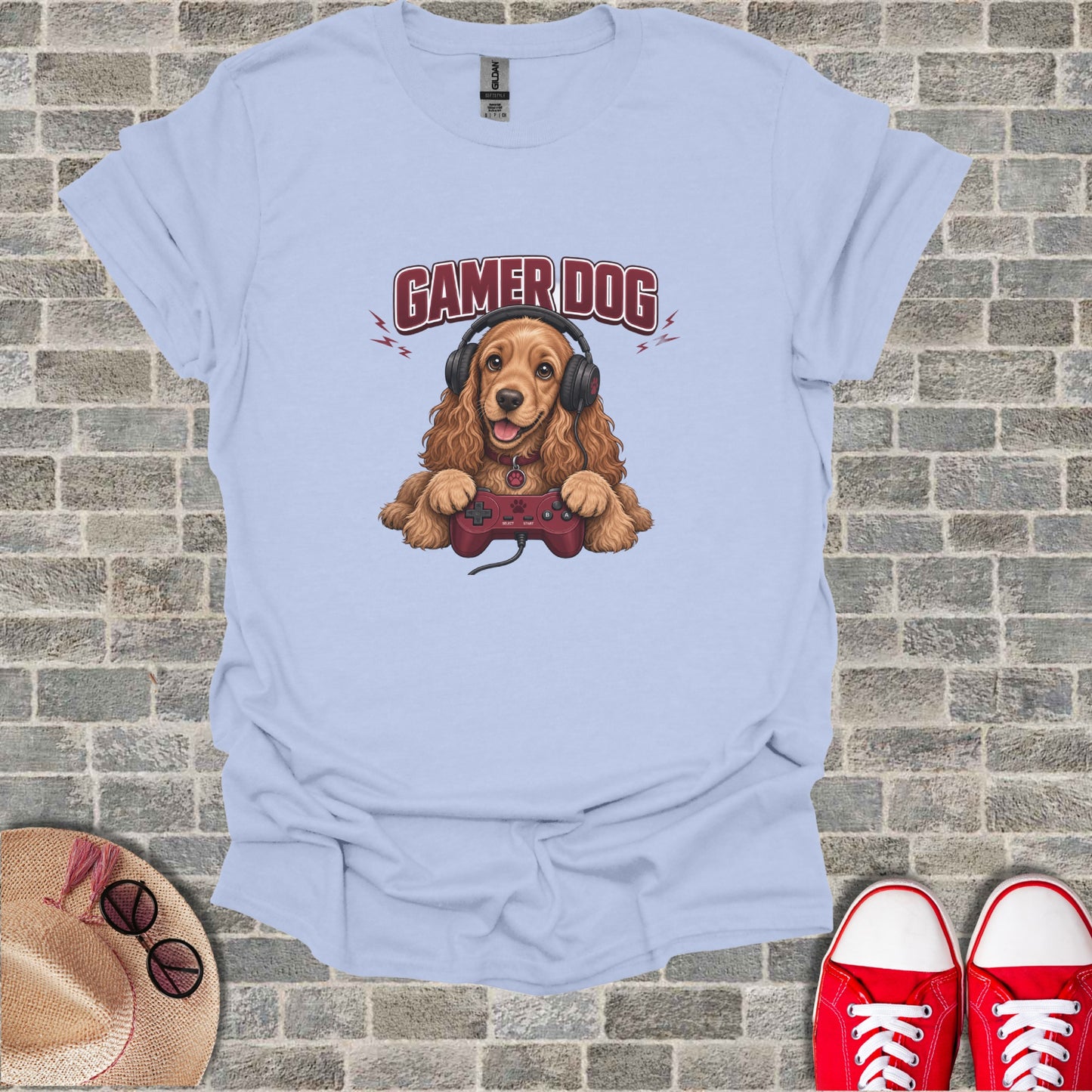 Light blue t-shirt with a cartoon cocker spaniel wearing headphones and holding a video game controller.