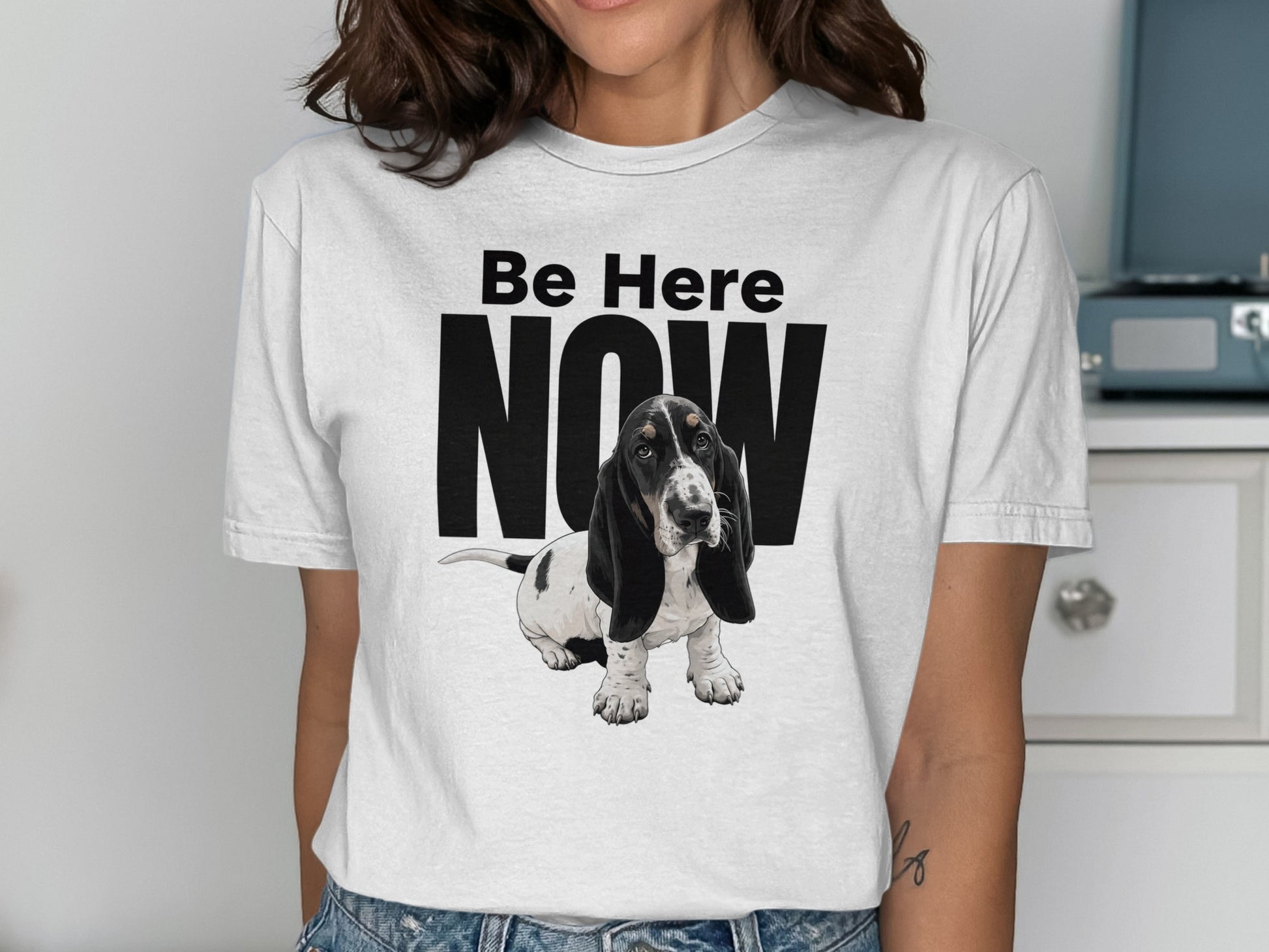Basset hound puppy on white t-shirt with "Be Here NOW" text.