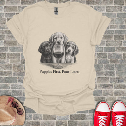 Cream t-shirt with black and white sketch of three puppies and a wine glass, text "Puppies First. Pour Later."
