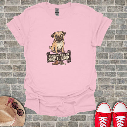 Pink t-shirt with a cartoon pug waiting for a shoe to drop.