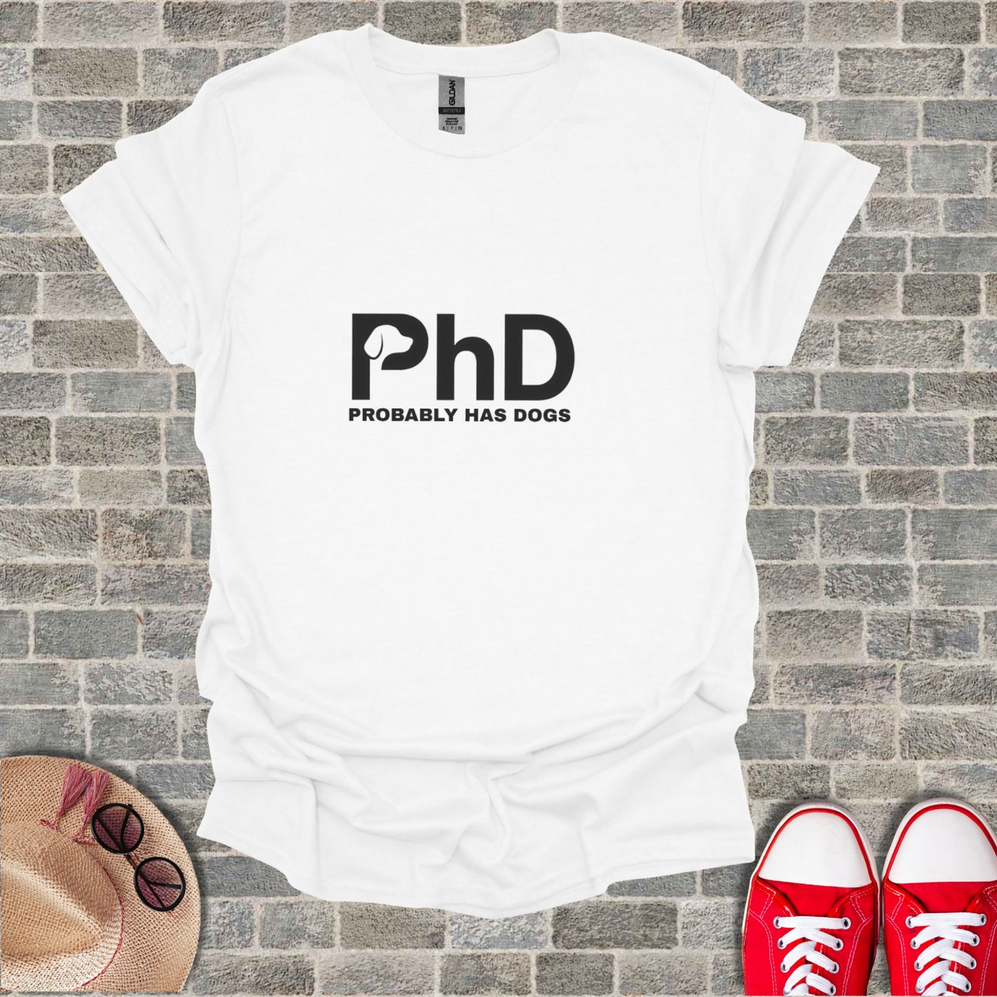 White t-shirt with "PhD PROBABLY HAS DOGS" graphic, laid flat with shoes and hat.