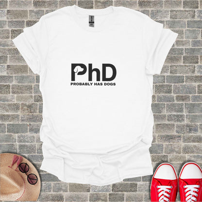 White t-shirt with "PhD PROBABLY HAS DOGS" graphic, laid flat with shoes and hat.