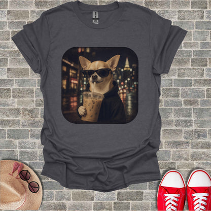 Chihuahua wearing sunglasses drinks an iced beverage in front of city lights.