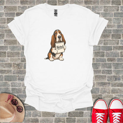 Basset Hound puppy holding a notepad with "Noted" written on it.
