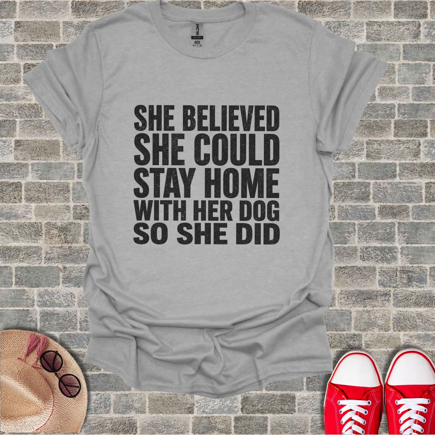 Gray t-shirt with black text "She believed she could stay home with her dog so she did."