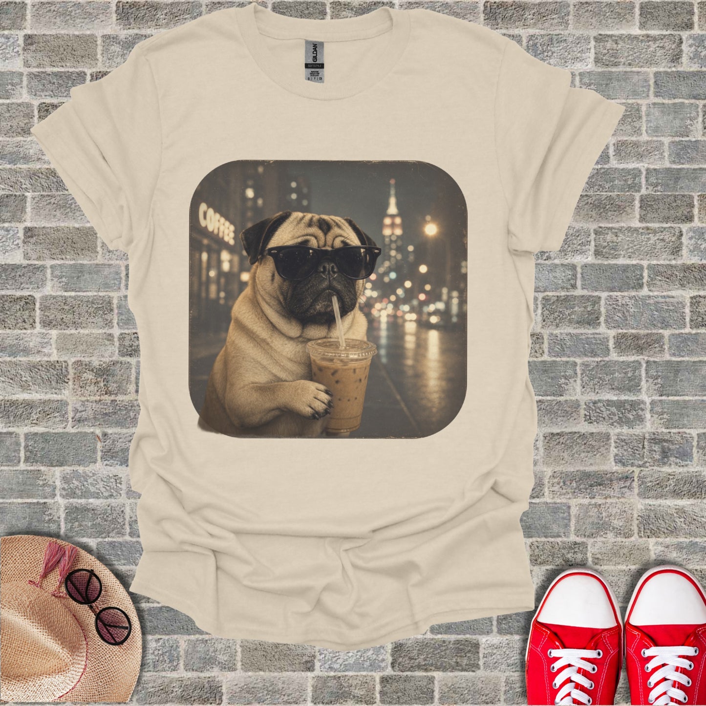 Pug wearing sunglasses drinks iced coffee in front of a city at night.