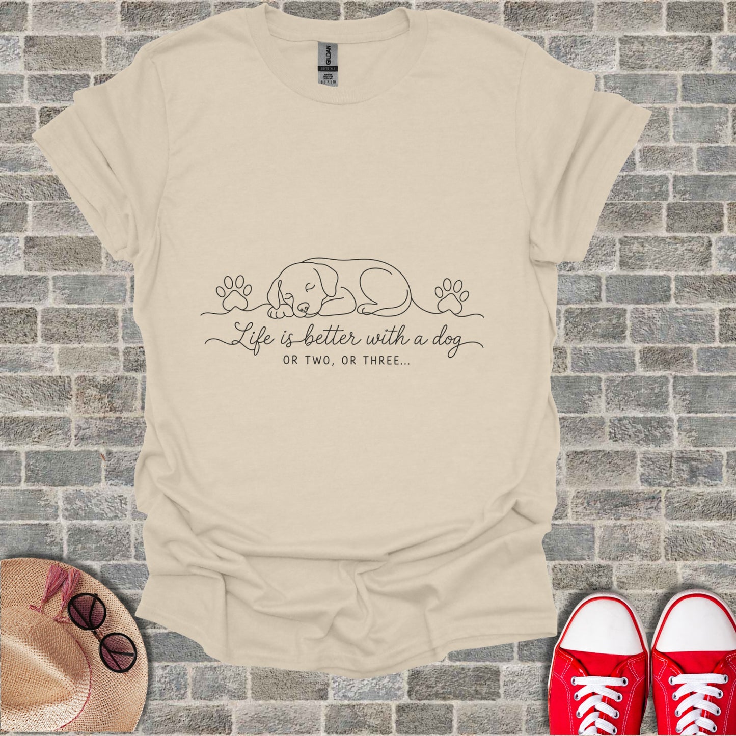 Cream t-shirt with line drawing of sleeping dog and paw prints. Text reads "Life is better with a dog OR TWO, OR THREE...".