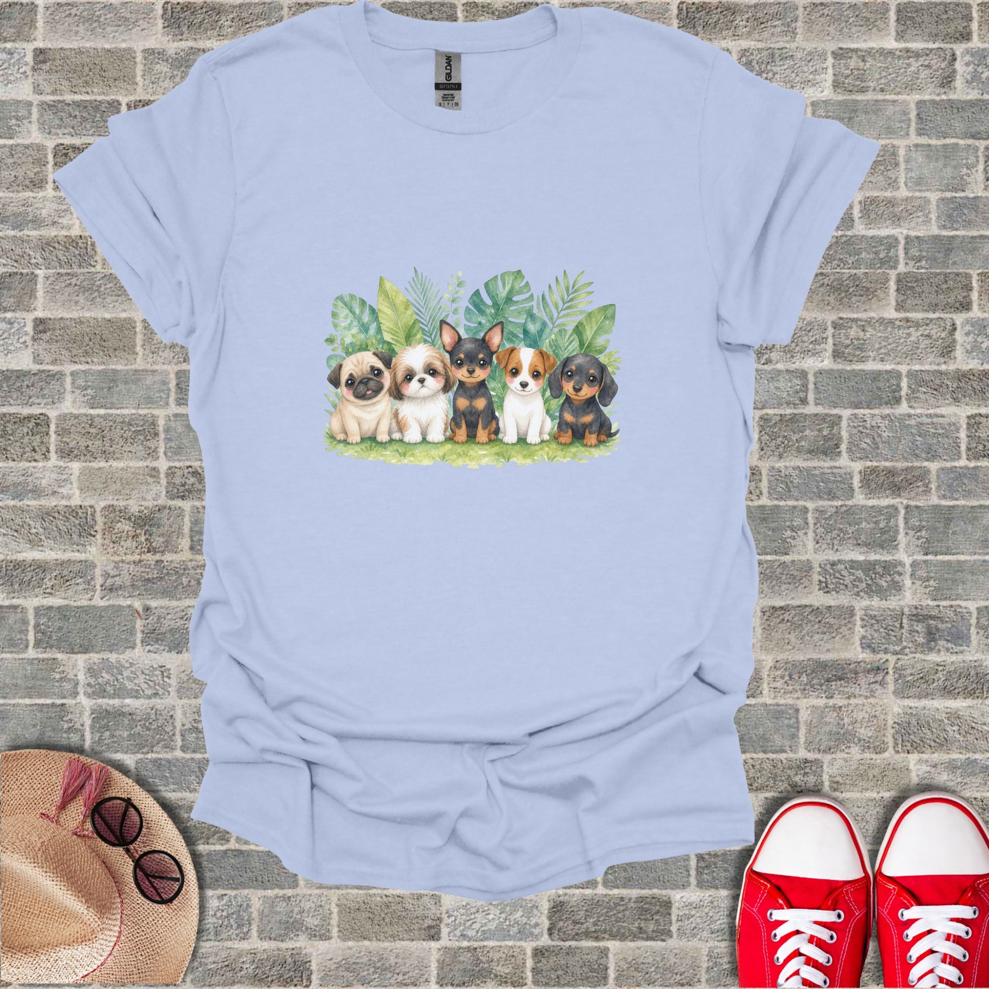 Five puppies sit in a line against a leafy background on a light blue t-shirt.