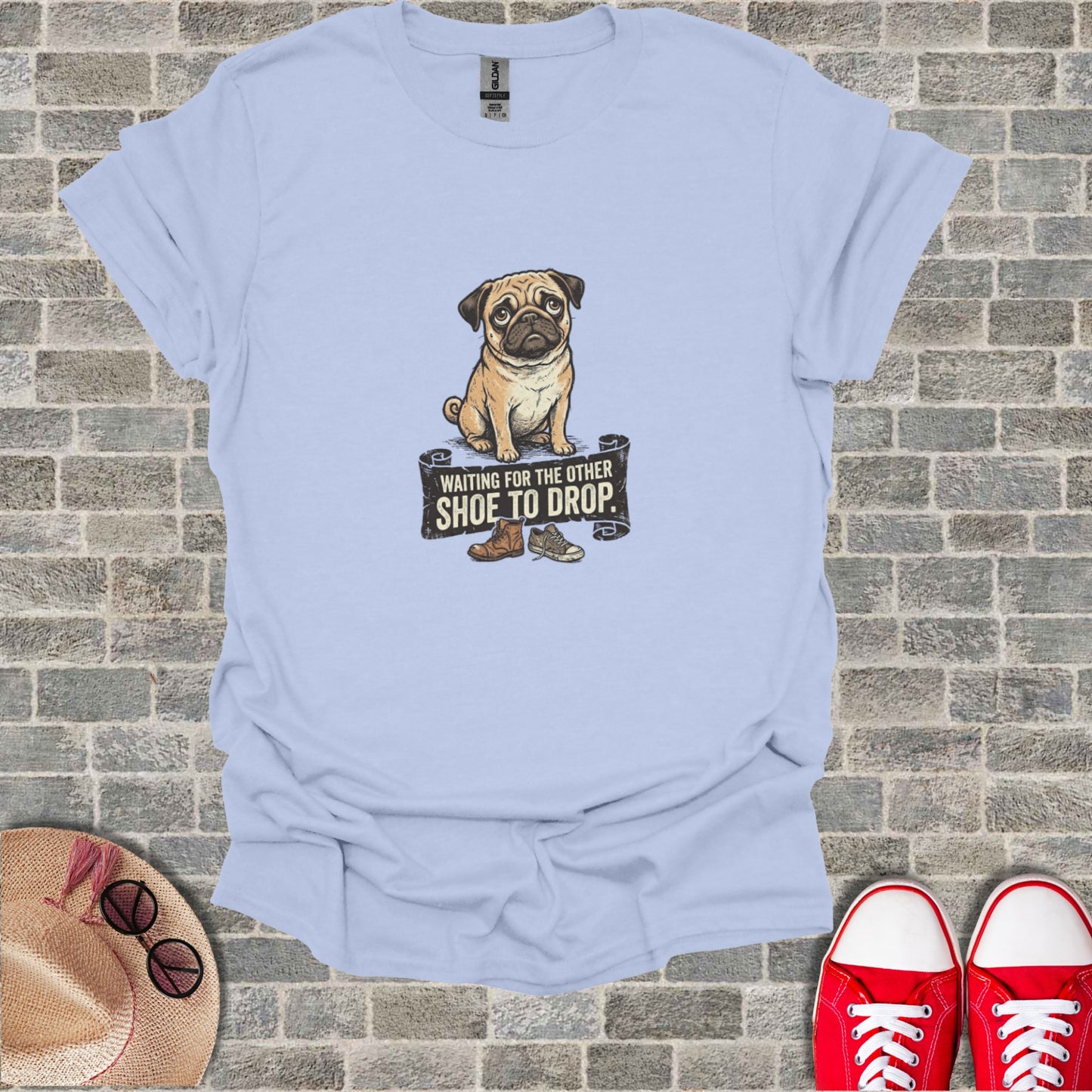 Light blue t-shirt with a pug sitting below a banner reading "Waiting for the other shoe to drop."