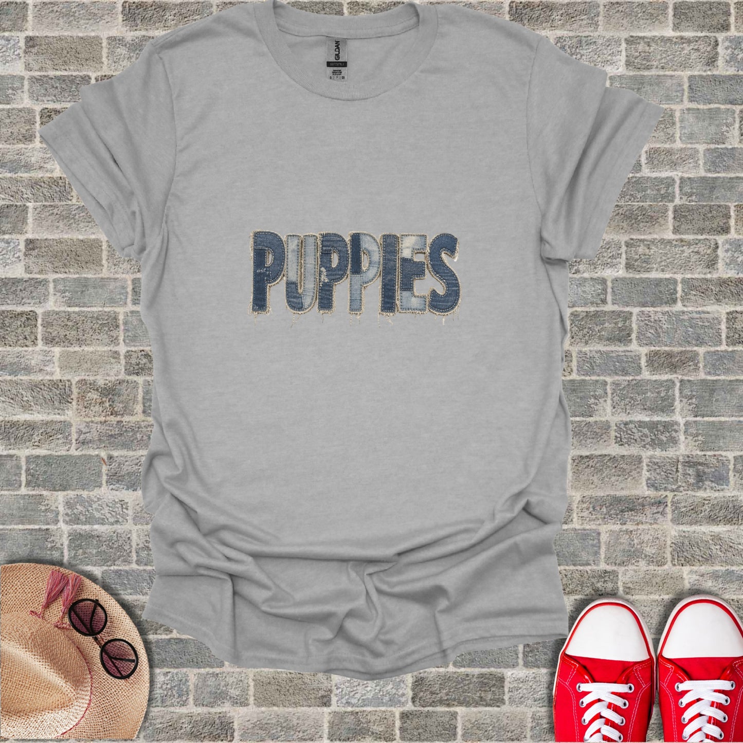 Gray t-shirt with "PUPPIES" in denim letters, near shoes and hat.