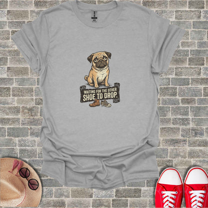 Pug sitting next to a sign that says "WAITING FOR THE OTHER SHOE TO DROP".