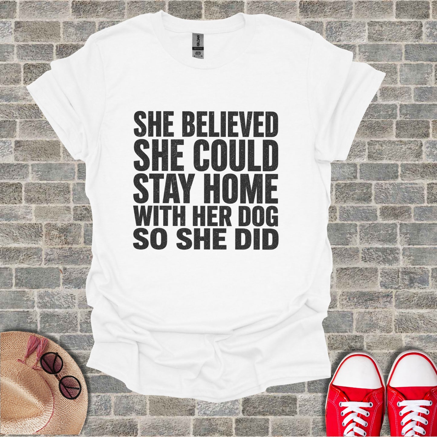 White T-shirt with black text: "She believed she could stay home with her dog so she did."