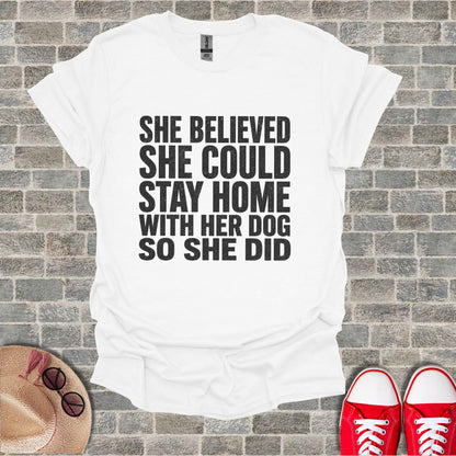 White T-shirt with black text: "She believed she could stay home with her dog so she did."