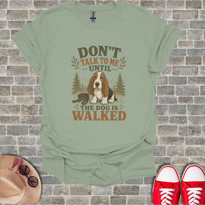 Basset hound wearing a bandana, text reads "Don't talk to me until the dog is walked."