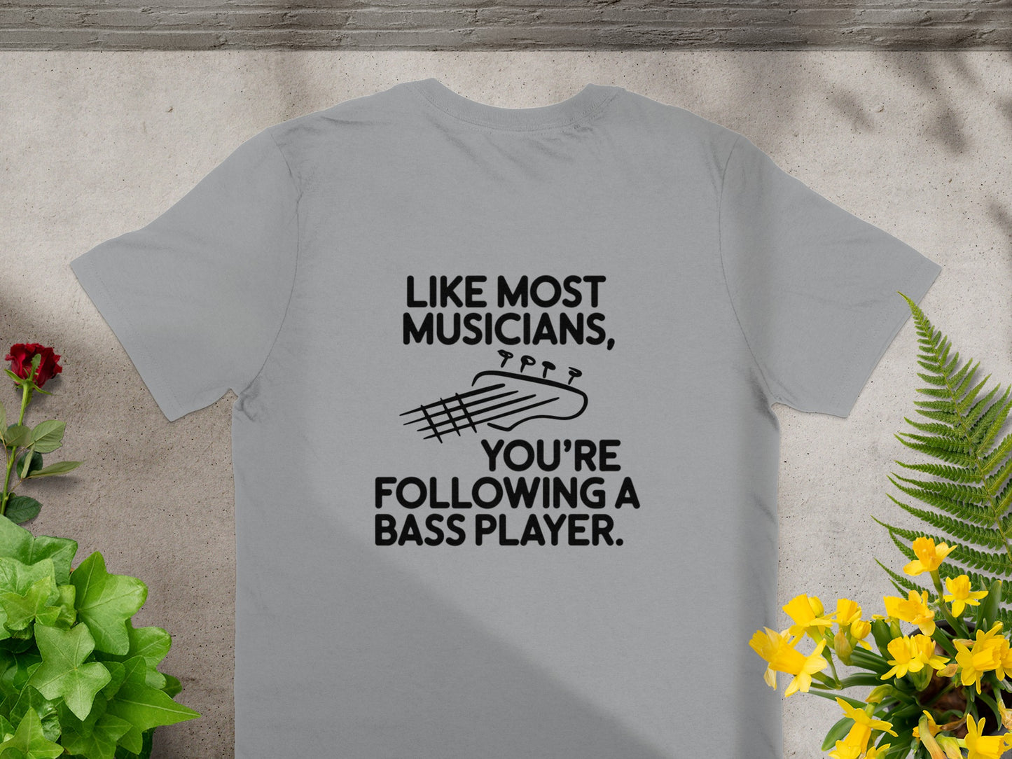 Grey t-shirt with black text and bass guitar graphic: "Like most musicians, you're following a bass player."