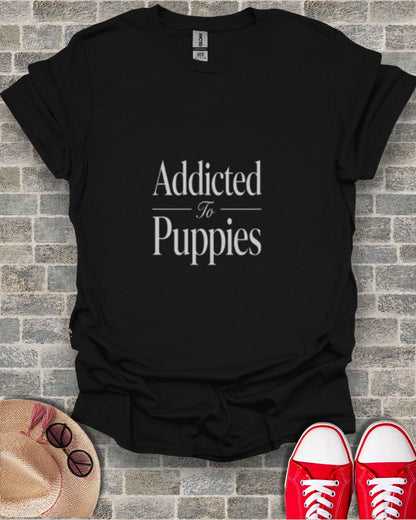Black t-shirt with "Addicted To Puppies" text, laid flat with hat and shoes.
