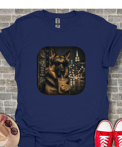German Shepherd wearing sunglasses drinks from iced coffee with city skyline behind.
