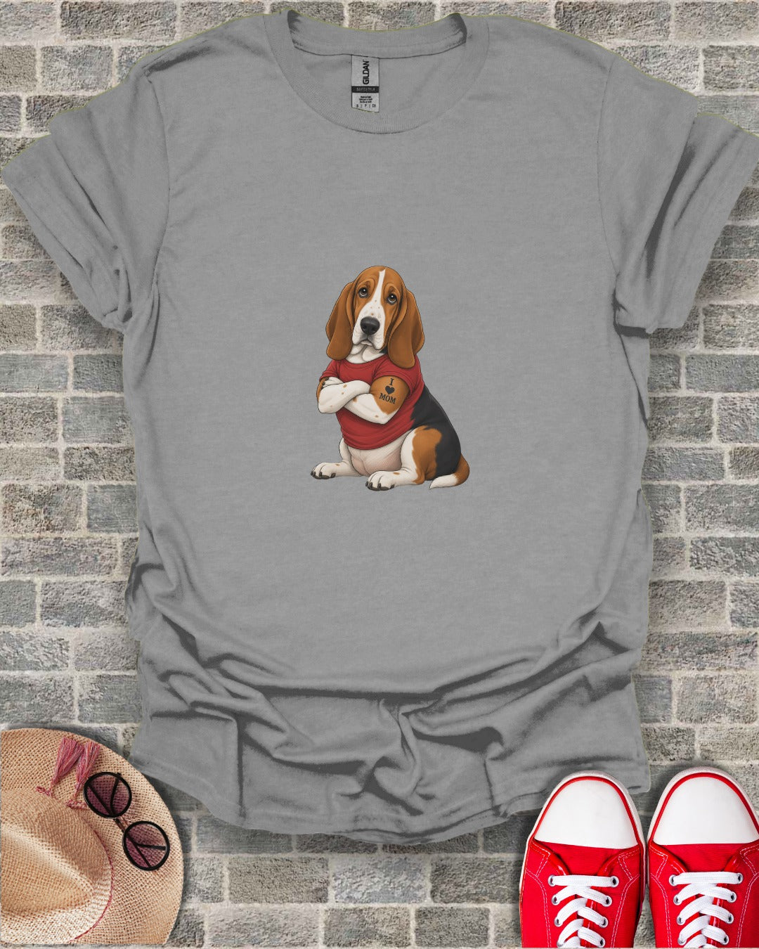 Basset hound wearing a red shirt with "MOM" on it, sitting.
