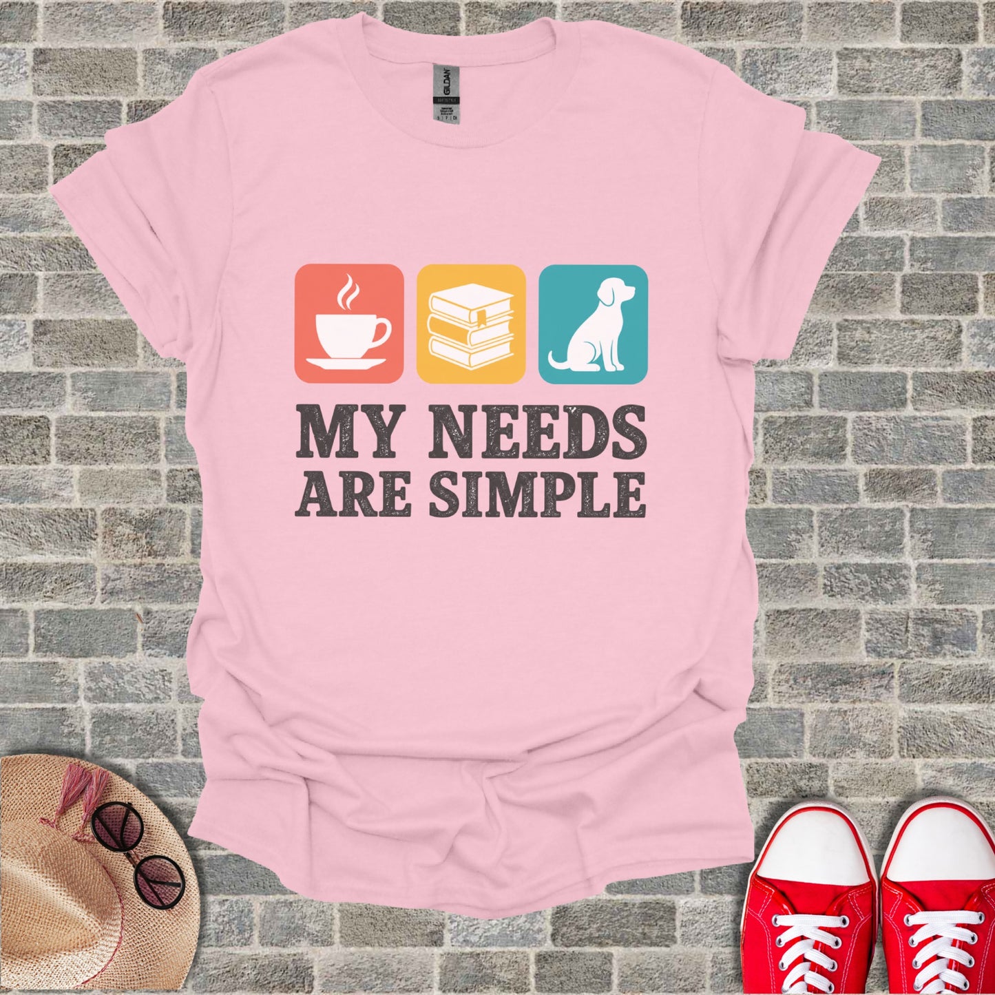 Pink t-shirt with three icons: coffee, books, dog. Text reads "MY NEEDS ARE SIMPLE".