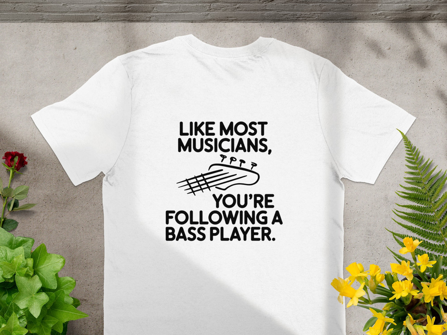 White t-shirt with black text and bass guitar graphic: "Like most musicians, you're following a bass player."