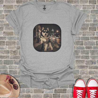 Husky dog wearing sunglasses sits and drinks from a straw in front of city lights.